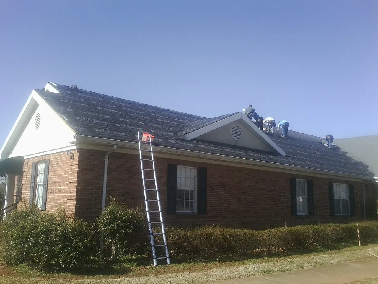 Crew tearing shingles off a brick ranch roof with a ladder set — Emergency Roof Repair work by our crew in Burnt Ranch