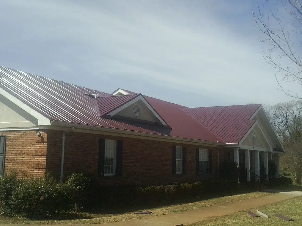 Red metal roof with gabled entries on a long brick building, from a Hail Damage Roof Repair job in Burnt Ranch
