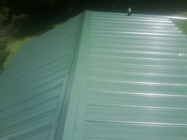 New green metal panels meeting at the ridge of a roof — Flat Roof Repair work by our crew in Burnt Ranch