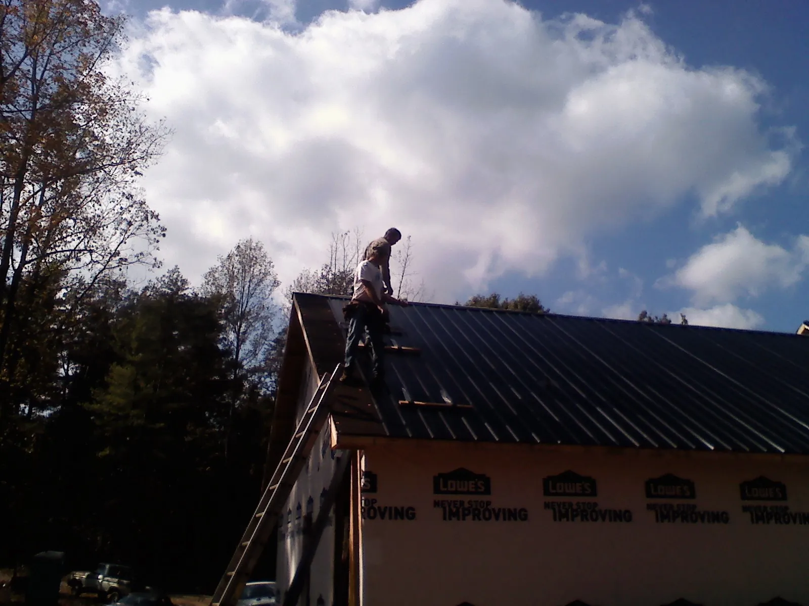 Roofer fastening dark metal panels high against a cloudy sky, from a Roof Inspection job in Burnt Ranch