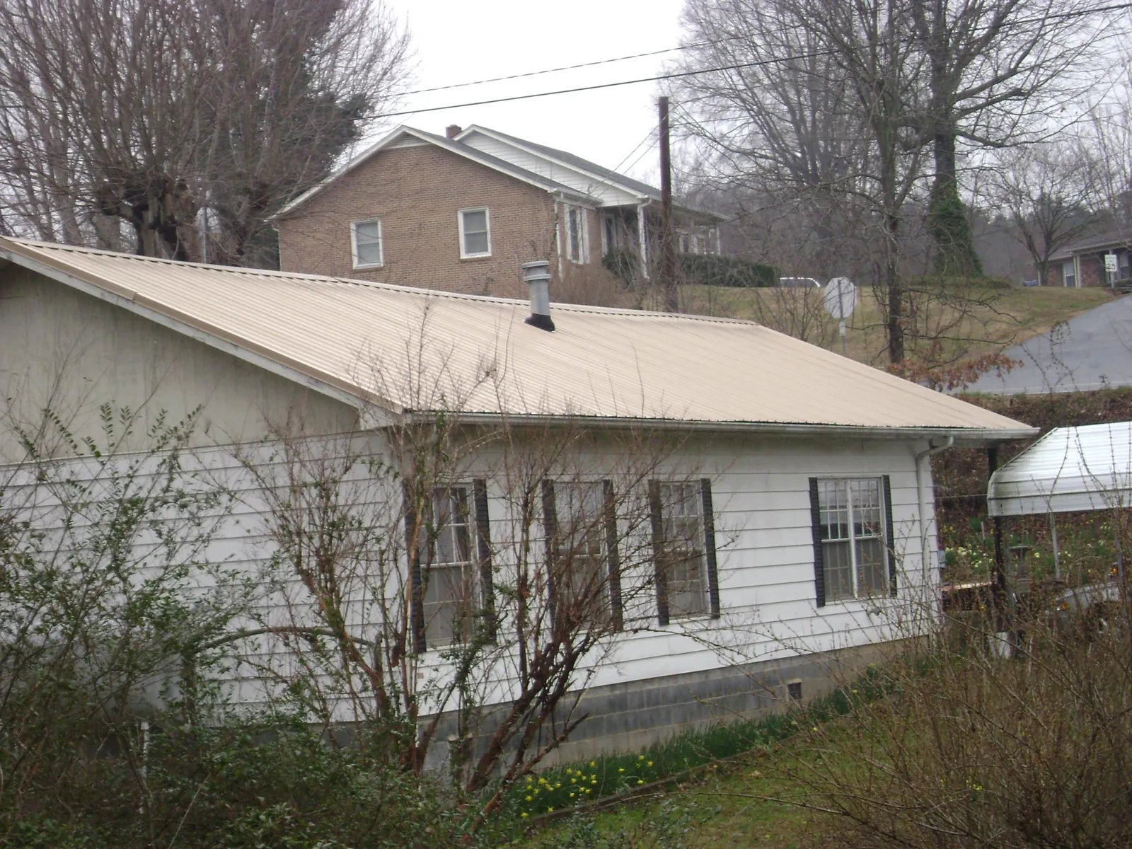 Tan metal roof on a white sided house set into a hillside — Commercial Roofing by Roofing Brothers in Burnt Ranch