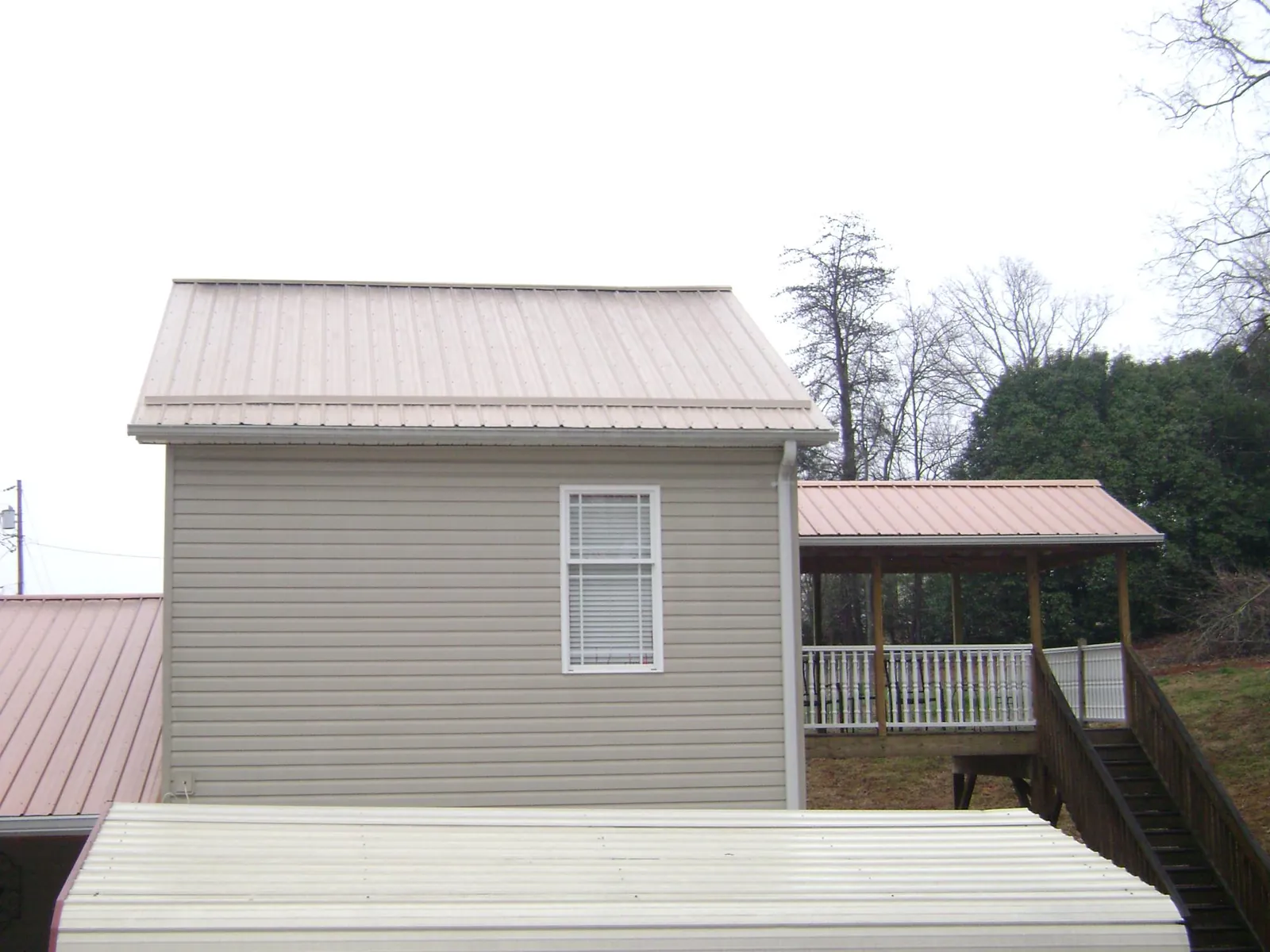 Tan metal roofs on a two story addition and attached porch, from a Roof Replacement job in Burnt Ranch